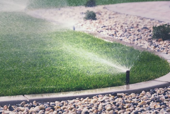 In-ground sprinkler head misting a green lawn